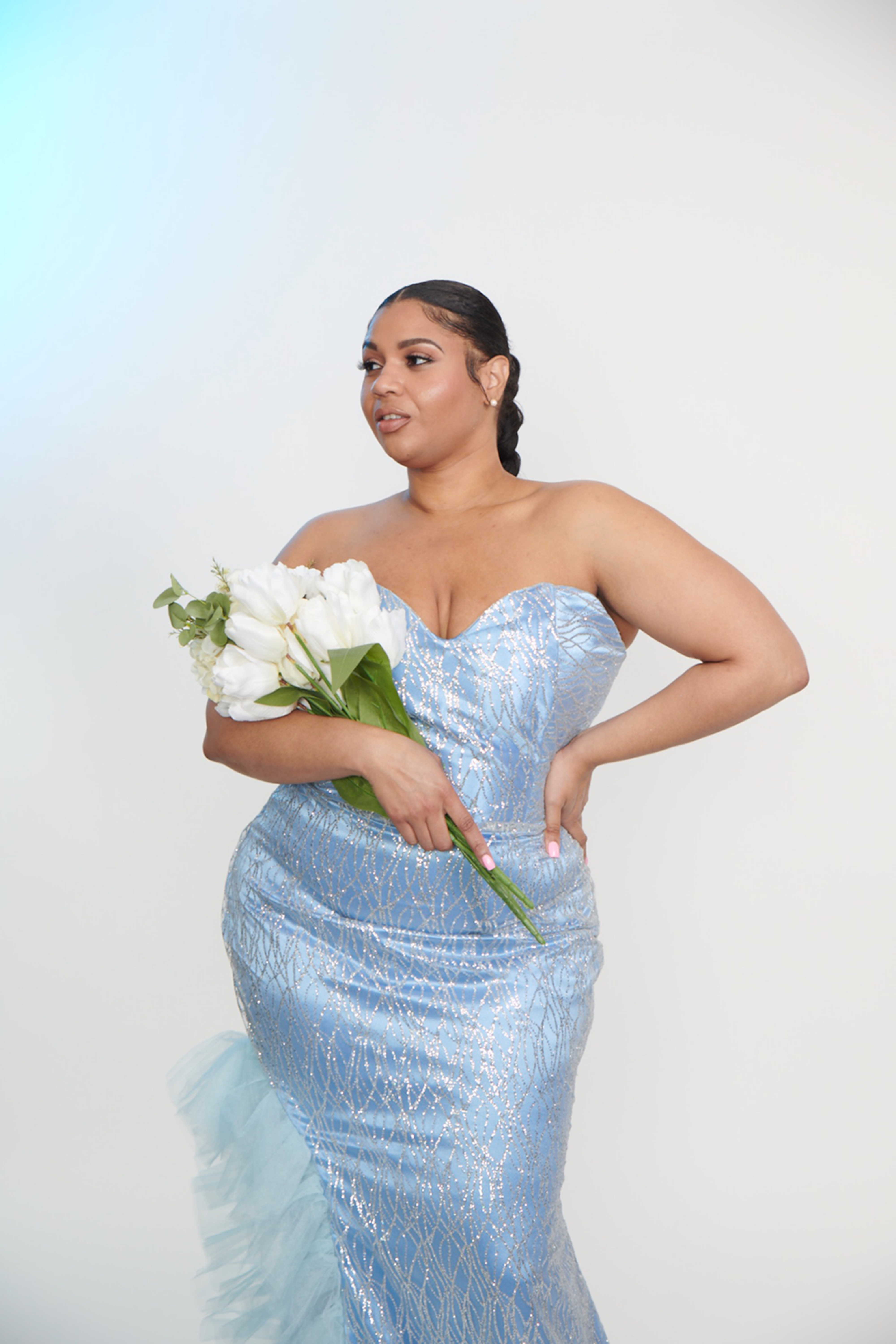 Woman in a light blue sequin gown holding white flowers against a white background